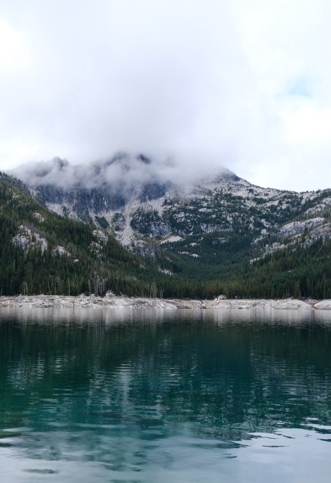 A blue lake with mountains and clouds above it.