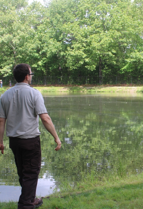 Service employee in refuge browns watches as young boy casts fishing pole into pond.