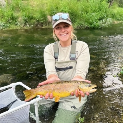 Image of Payton Hanssen holding a fish next to a stream.