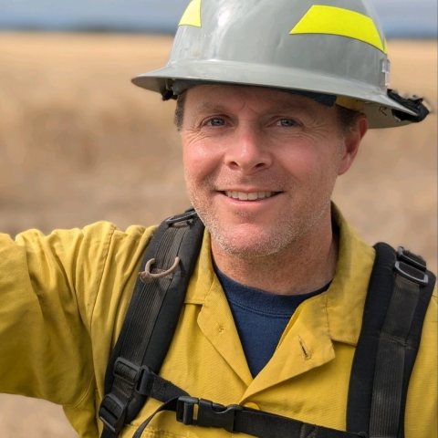 A close up of a person wearing firefighting gear looking at the camera