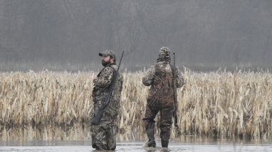 An image of two hunters walking in water. 