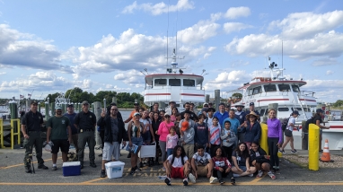 Group of people smiling at camera in front of big charter fishing boat. 