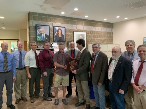 A person flanked by others receives a plaque