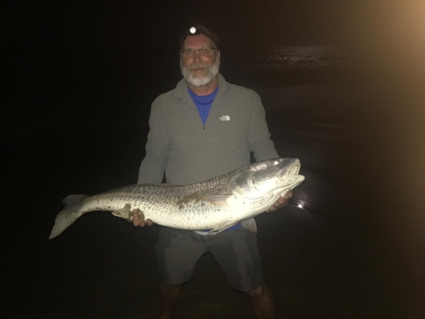 Angler holding large red drum fish at night