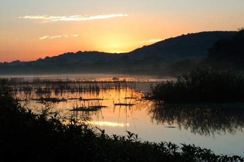 Sunset behind mountains that overlook a marsh framed by low vegetation. 