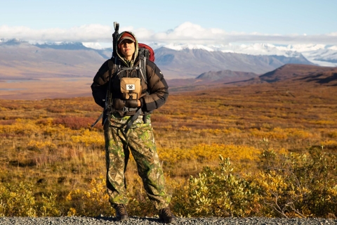 A hunter in camo with big mountains towering in the background. 