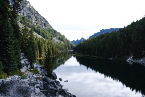 A scene of a very calm lake reflecting trees and mountains surrounding it