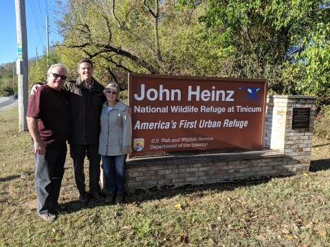 Three people stand next to a welcome sign at John Heinz NWR