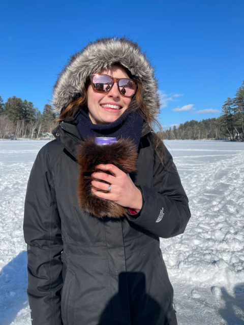 Woman wearing a winter coat in a snowy field holds a beverage koozie made from beaver fur. 