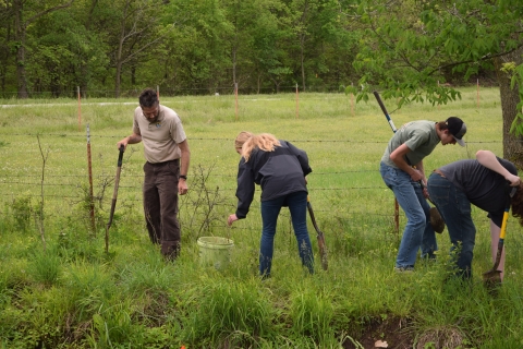 High school students and Fish and Wildlife Service staff holding shovels and planting small trees