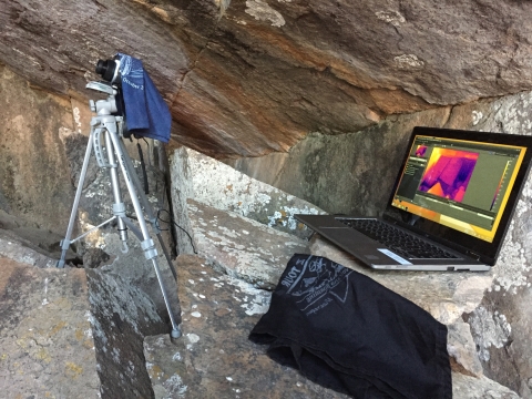 a camera on a tripod next to a laptop computer displaying an infrared image on the screen