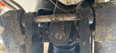 A close-up of black plastic and a metal hinge covered in brown fibers and invasive mussel shells.