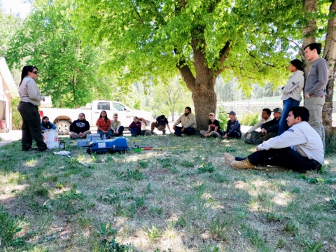 A woman in a fish and wildlife service uniform stands towards about a dozen people with some standing and some sitting