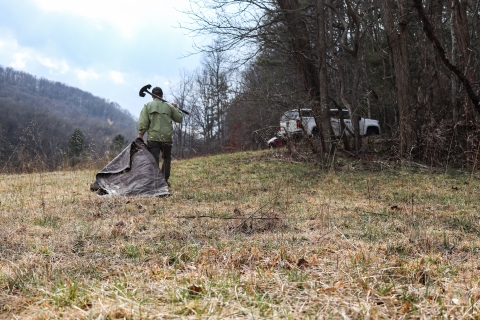 Man walking across a field, dragging a tarp and carrying a shovel over his shoulder