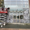 Two people on a construction lift apply decals to the front of a building