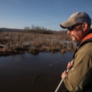 Biologist stands on the front of a boat with net to catch fish. 