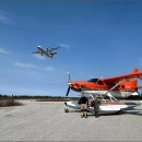 plane flying over two pilot biologists standing in front of a plane
