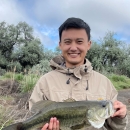 Ywj Pheej Yang holding a largemouth base with a natural setting in the background