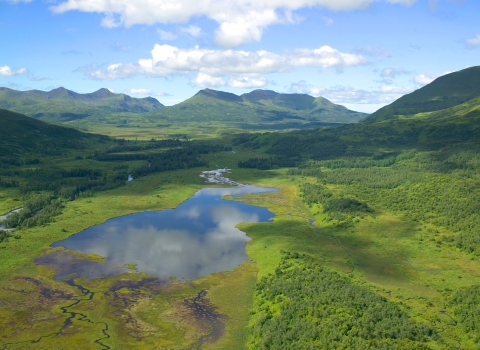 Clouds reflect in a wetland surrounded by mountains.