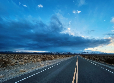 An empty road heads into the distance while dark, ominous clouds fill the sky above