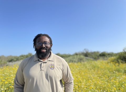 A man wearing a long sleeved polo stands in front of a field with golden flowers