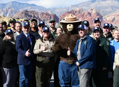 A group of uniformed officials pose with a Smokey mascot